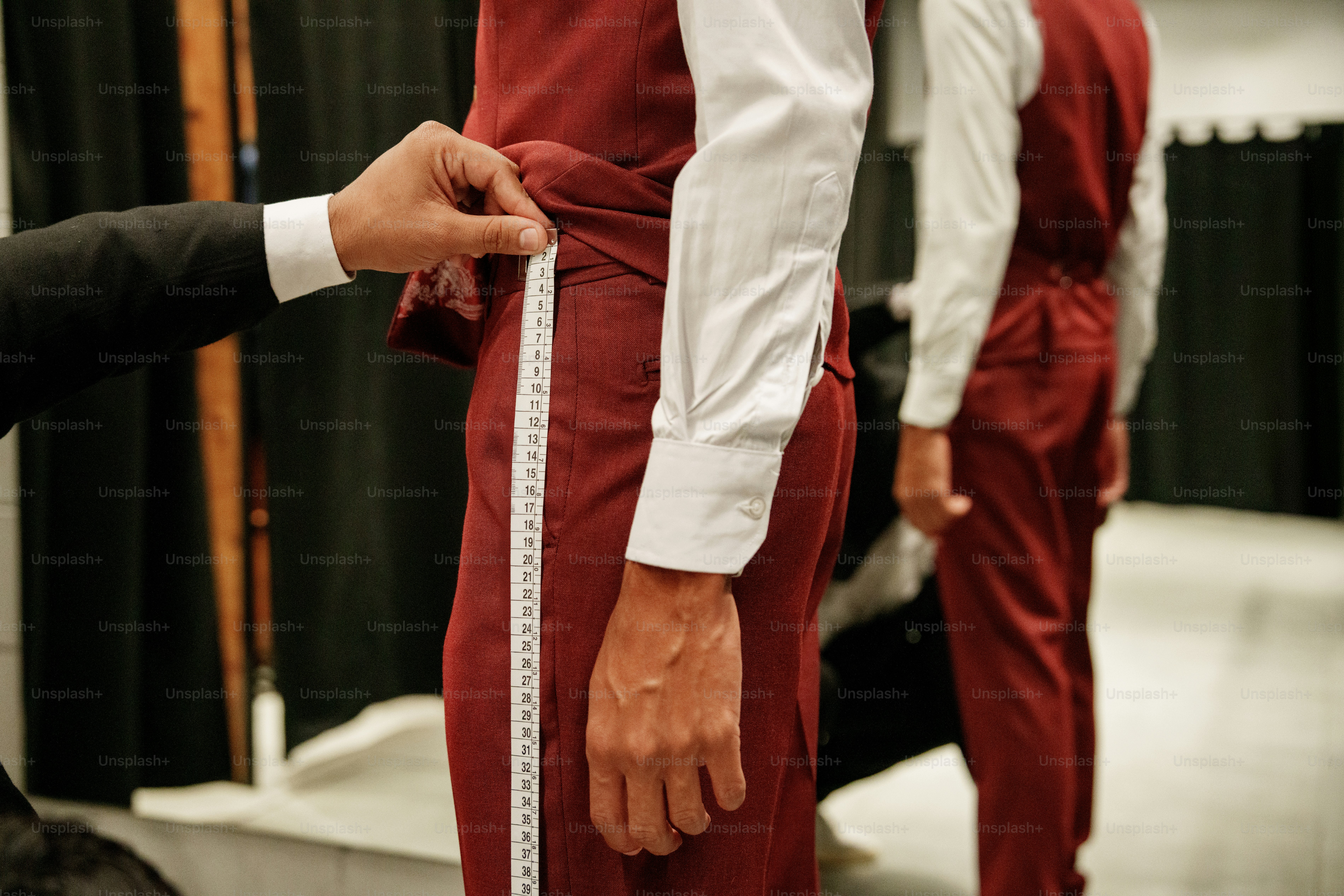 Tailor measuring burgundy pants on a person